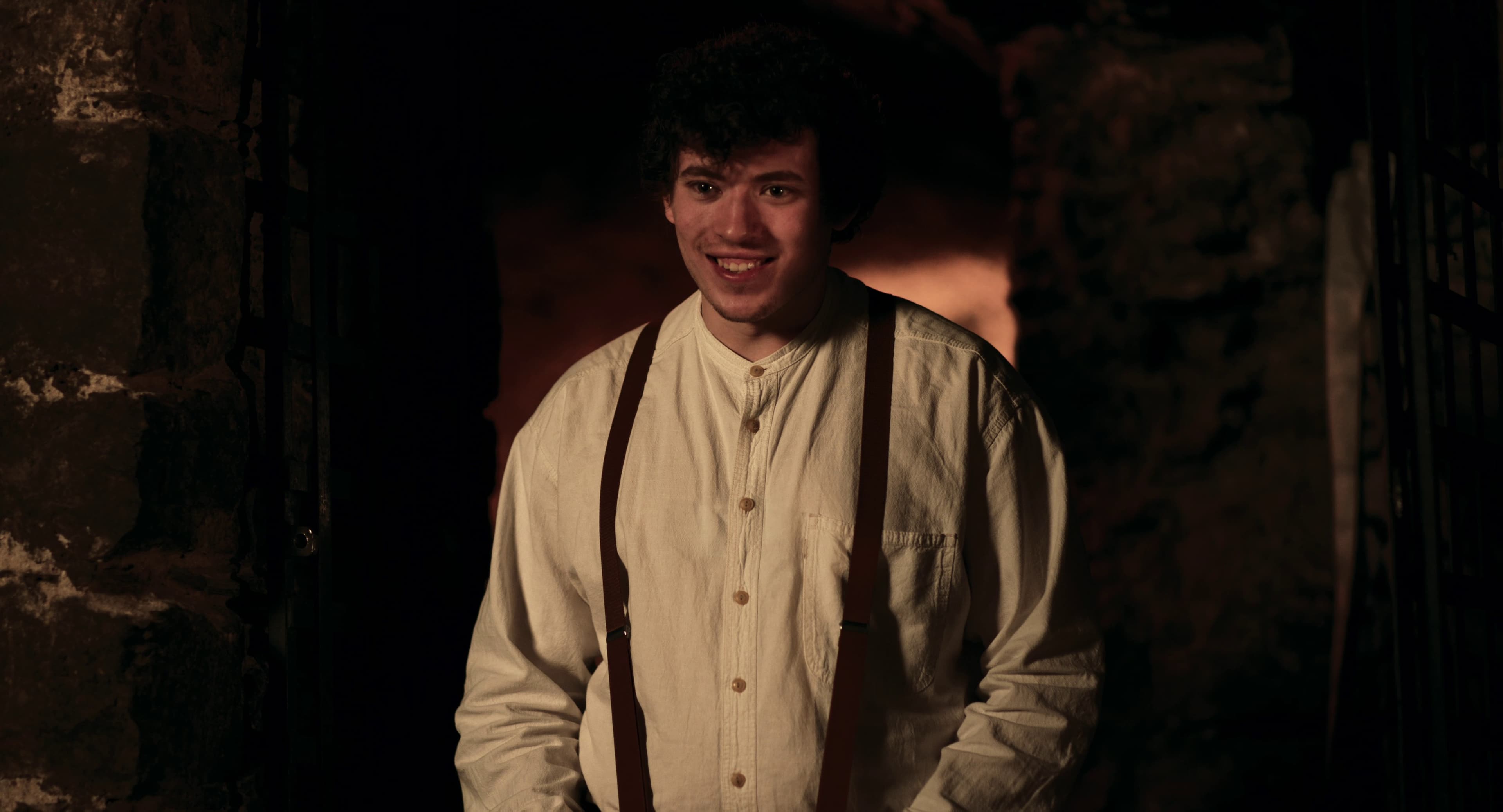 A smiling young man in a white shirt and suspenders